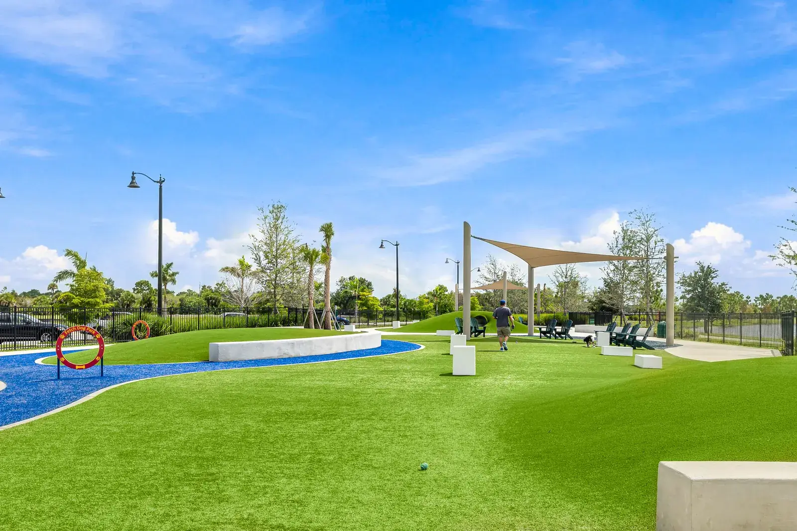 Open dog park lawn with a curving blue path and a shade sail in Wellen Park