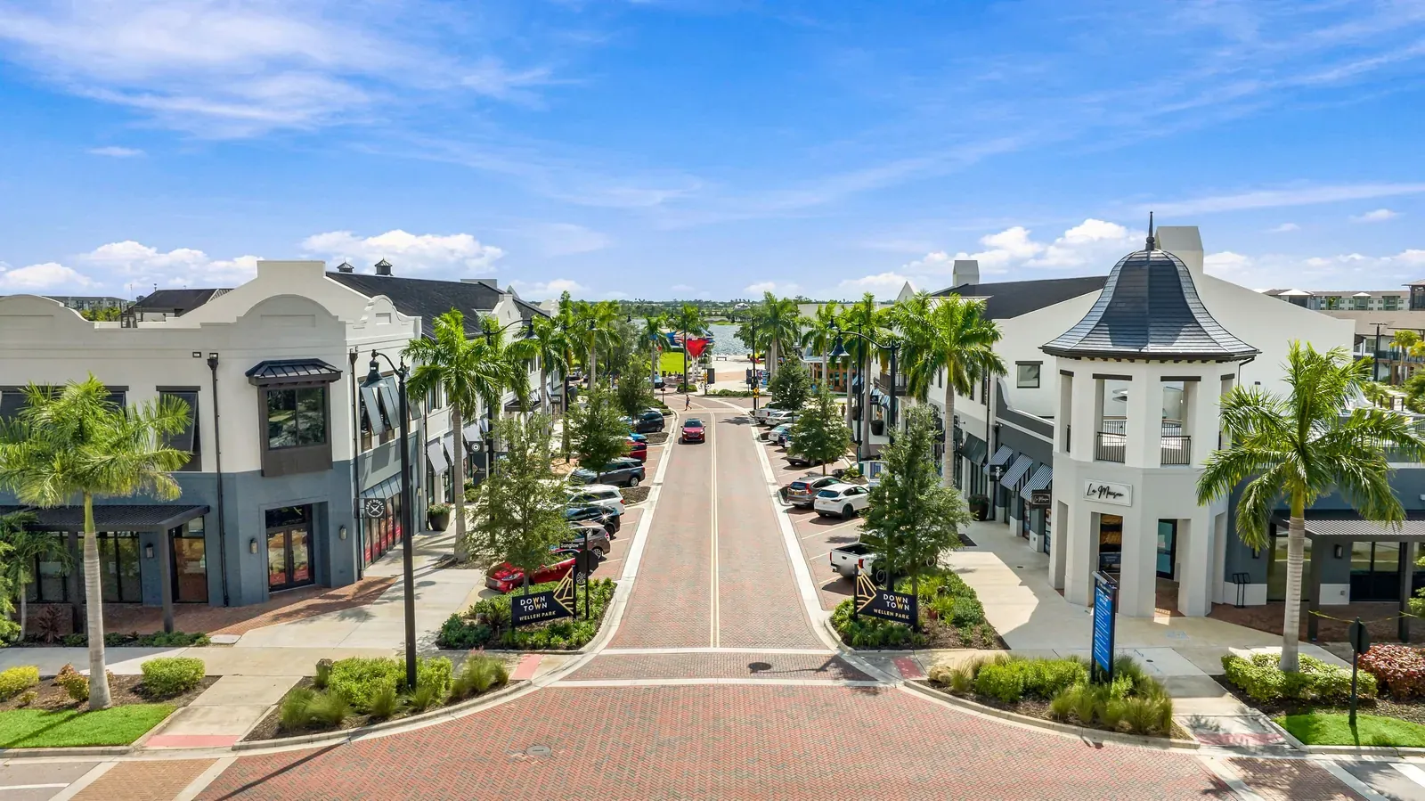 Daytime view from above of a palm-lined main street with shops and a cupola-topped corner building in Downtown Wellen Park